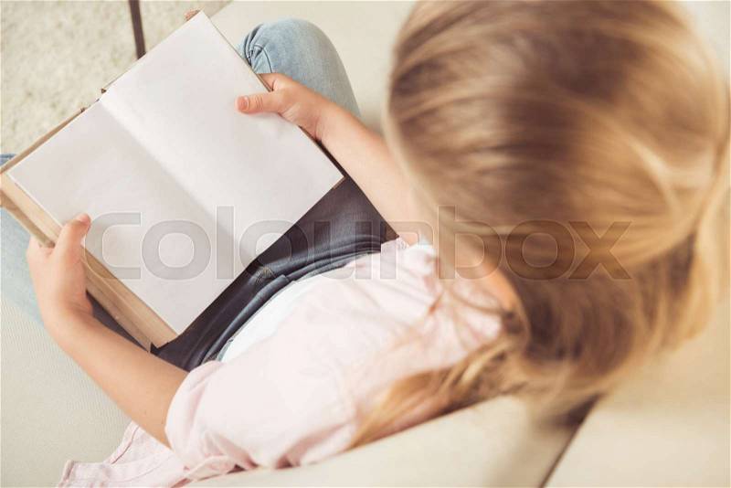 Overhead view of schoolgirl holding empty book while sitting on sofa at home, stock photo