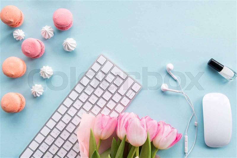 Top view of keyboard, macarons, nail polish, earphones and bouquet of flowers isolated on blue, stock photo