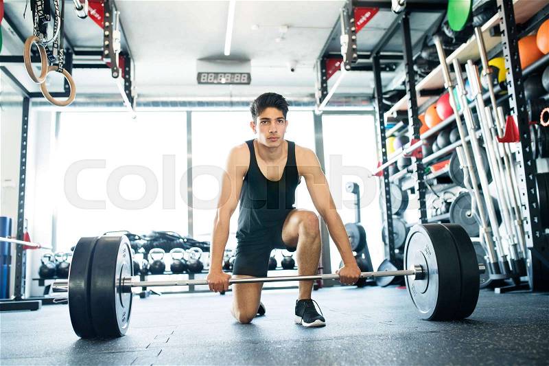 Young fit hispanic man in gym lifting heavy barbell, flexing muscles, stock photo