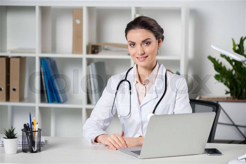 Young caucasian doctor using laptop and looking at camera in clinic, stock photo