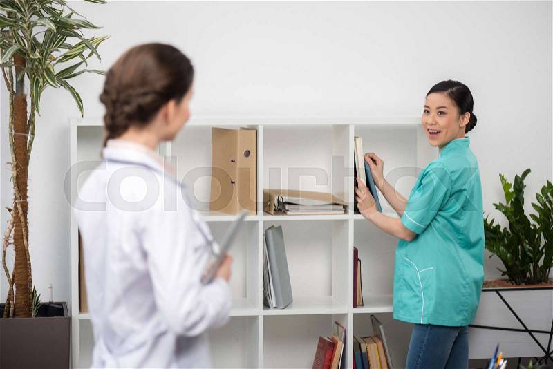 Smiling internist talking with doctor in clinical office, focus on background, stock photo