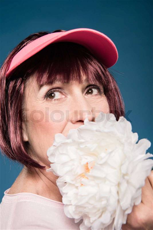 Beautiful elderly woman holding and smelling white flower while looking away, stock photo