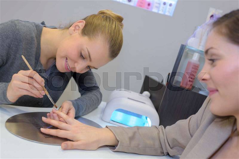 Attractive nail salon worker giving a manicure to customers, stock photo