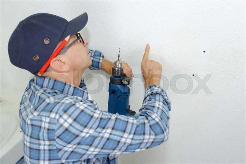 Seniro worker makes a hole in wall with drill, stock photo