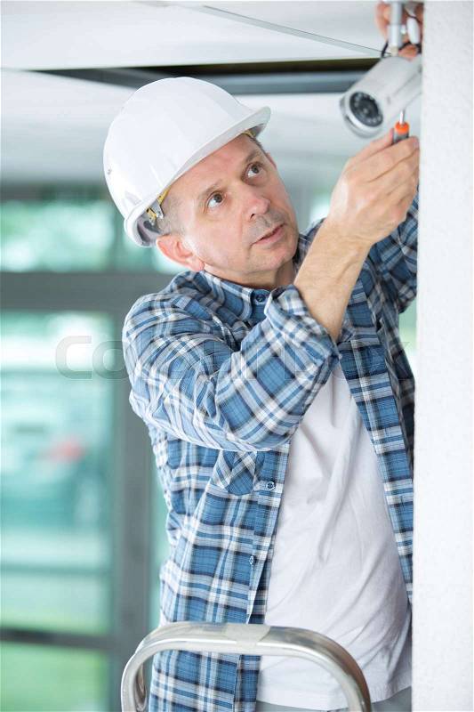 Mature male technician installing camera on wall with screwdriver, stock photo