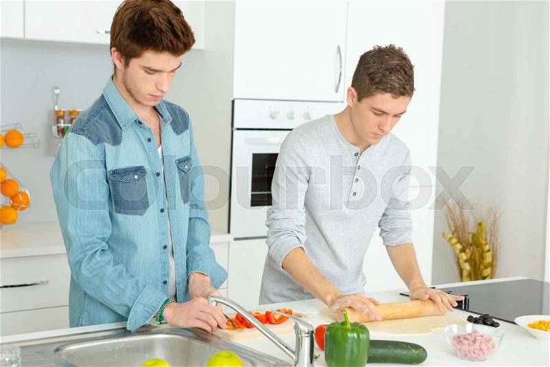 Three male friends making pizza in kitchen together, stock photo