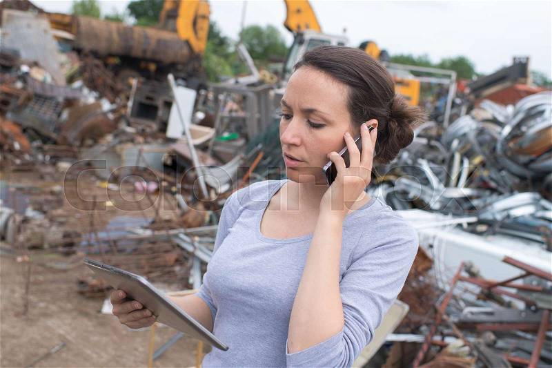 Beautiful brunette on the phone at junk yard, stock photo