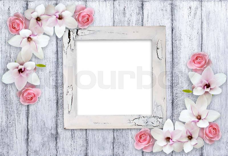 Retro empty photo frame with magnolia flowers and roses on background of shabby wooden planks in rustic style, stock photo