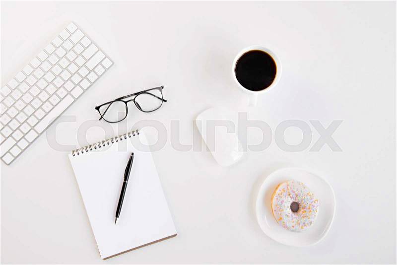 Top view of blank notebook with pen, eyeglasses, keyboard, computer mouse, cup of coffee and tasty doughnut at workplace, stock photo