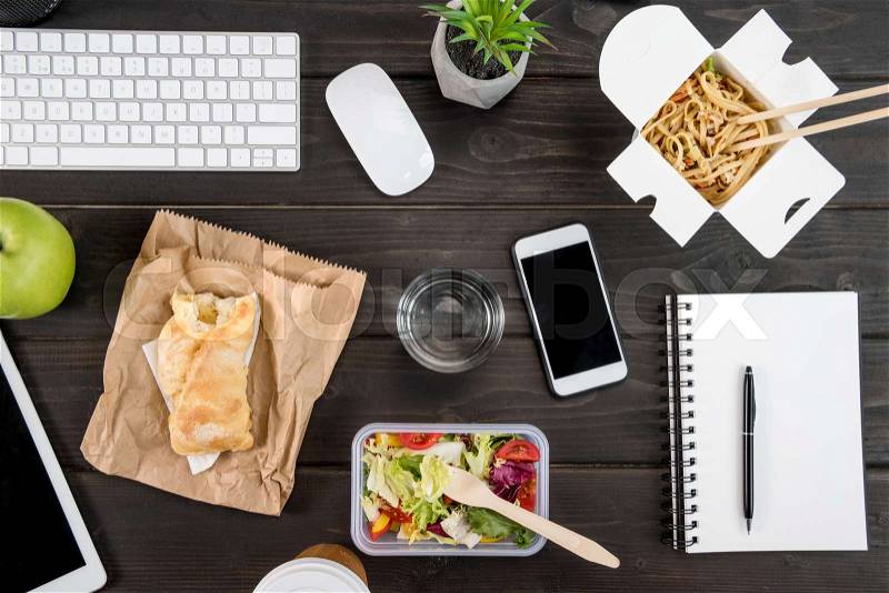 Top view of digital devices with food with glass of water mock-up on tabletop, stock photo