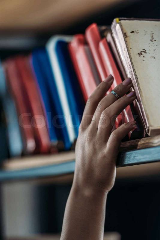Cropped shot of student holding book at bookshelf in library , stock photo