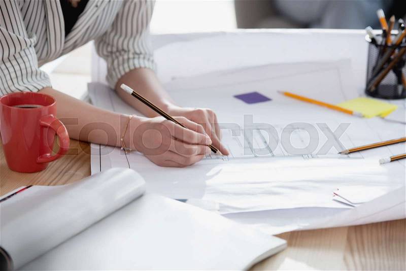 Cropped shot of businesswoman holding pencil and working with blueprint, stock photo