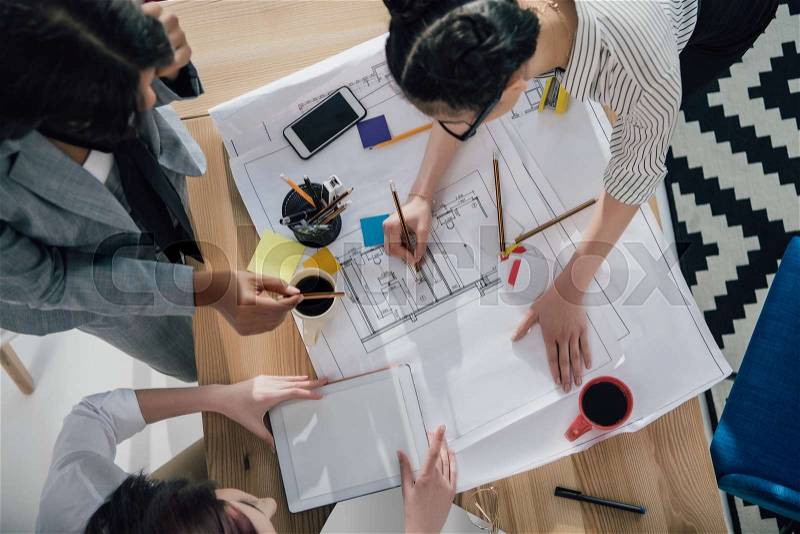 Overhead view of professional young architects working with blueprints and digital tablet, stock photo
