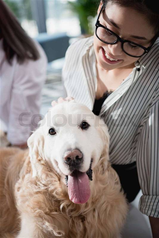Portrait of young smiling asian businesswoman petting dog at office, stock photo