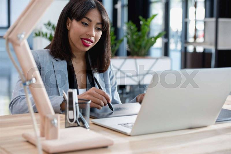 Young african american designer working with drawing tablet and laptop at office, stock photo