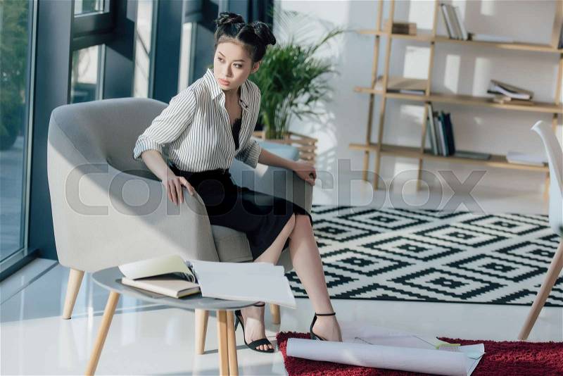 Serious asian businesswoman sitting in chair and looking away in office, stock photo