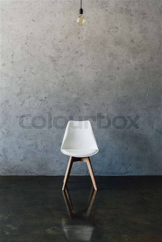Electric bulb and modern white chair on the floor at empty room, stock photo