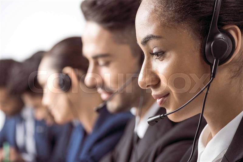 Close-up view of smiling call center operator in headset working with colleagues behind , stock photo