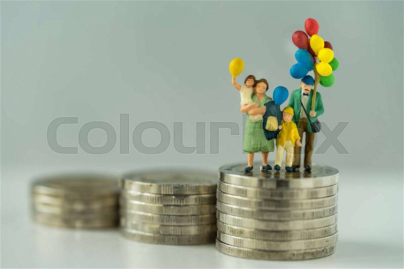 Miniature figure family holding balloon standing on stack of coins as financial business or happy concept, stock photo