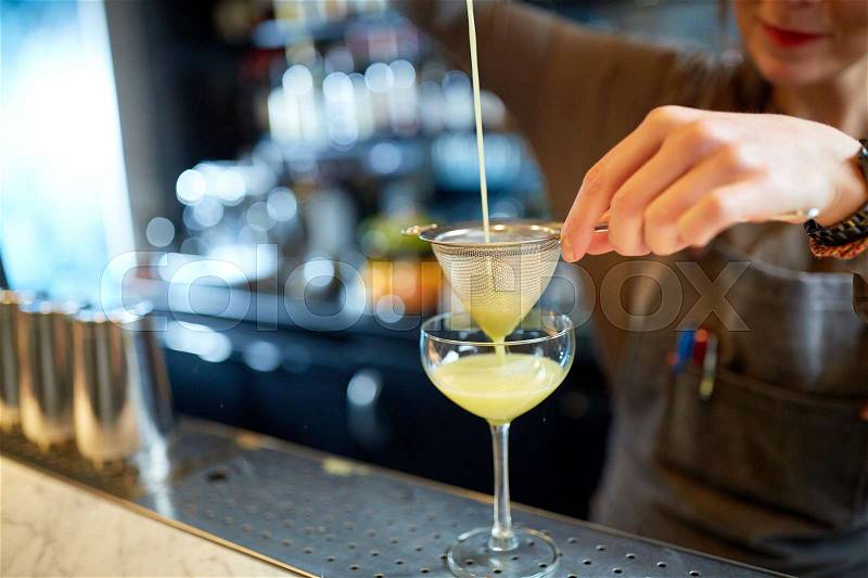 Alcohol drinks, people and luxury concept - woman bartender poring cocktail through strainer into glass at bar, stock photo