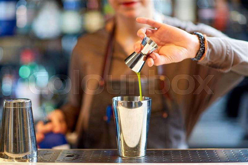 Alcohol drinks, people and luxury concept - woman bartender with jigger pouring syrup into shaker and preparing cocktail at bar counter, stock photo