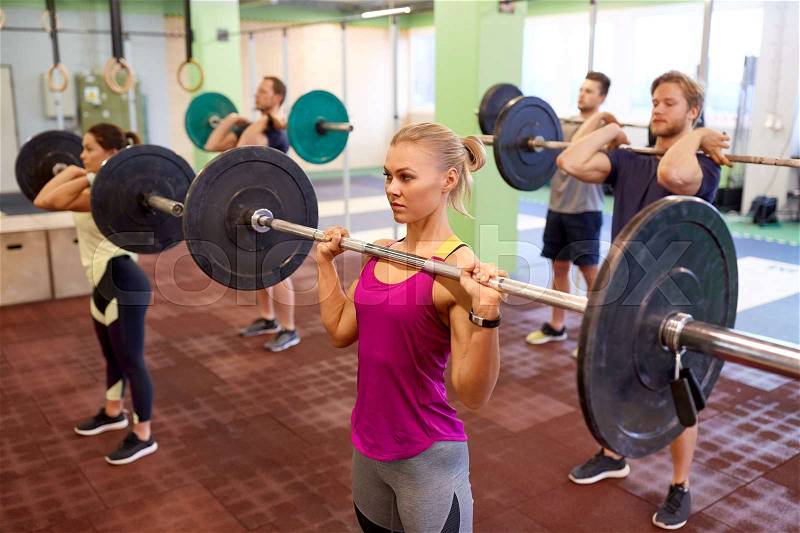 Fitness, sport, training, exercising and lifestyle concept - group of people with barbells doing shoulder press in gym, stock photo