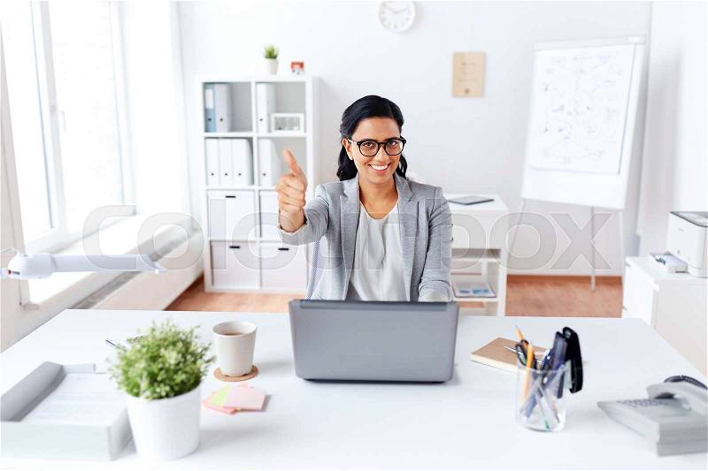 Business, people and success concept - happy smiling businesswoman with laptop computer showing thumbs up at office, stock photo
