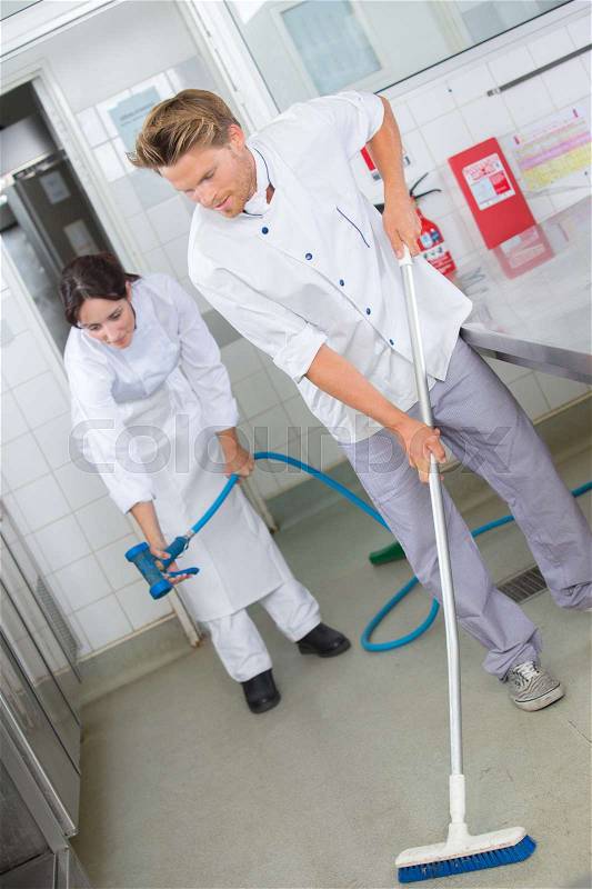 Restaurant employees cleaning the kitchen floor, stock photo
