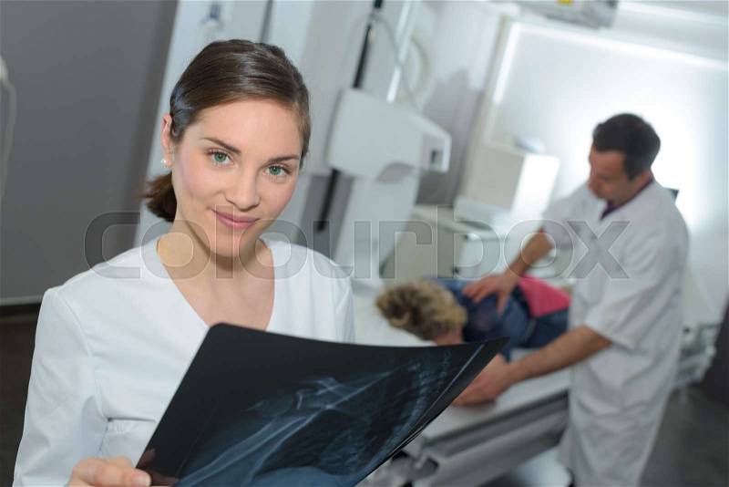 Female doctor with x-ray doctor and patient in the background, stock photo