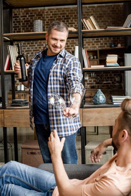 Smiling man giving glass of wine to his boyfriend at home, stock photo