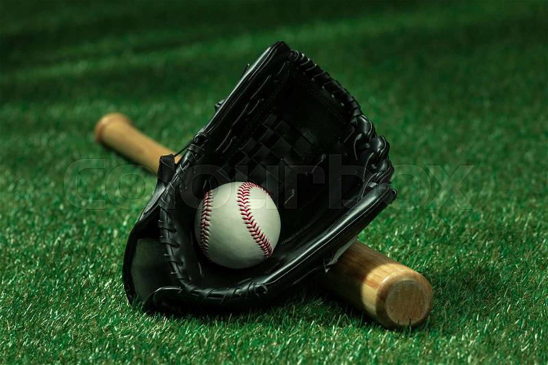 Closeup view of baseball bat, glove and ball lying on green field , stock photo