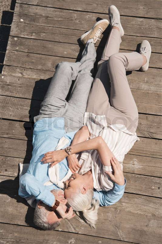 Above view of senior couple hugging while lying on wooden pavement, stock photo