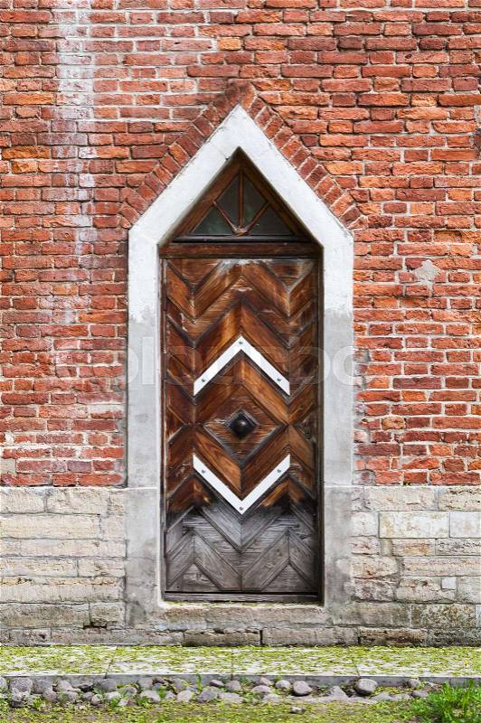 Dark wooden door in red brick wall, Gothic Revival architecture style. Background texture, stock photo