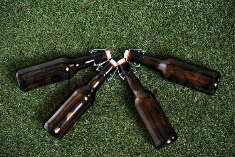 Top view of four closed beer bottles lying together on green grass, stock photo
