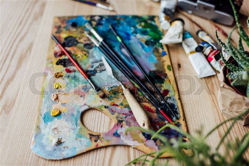 High angle view of artist palette with paint brushes, palette knife and oil paint tubes on the table, stock photo