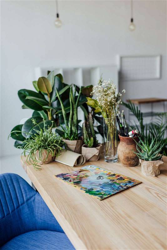 Wooden table full of potted green plants and art supplies , stock photo
