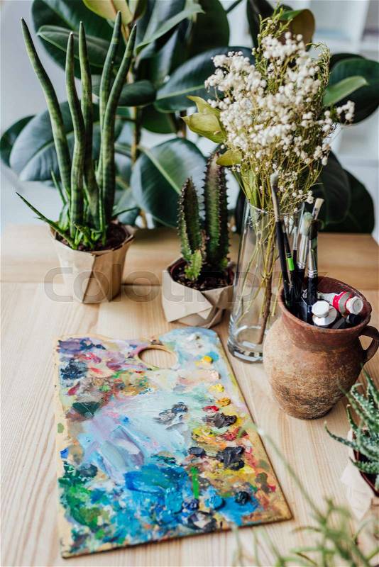 Wooden table full of potted green plants and art supplies , stock photo