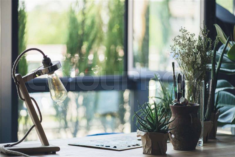 Group of potted green plants, drawing equipment and retro table lamp on workplace, stock photo