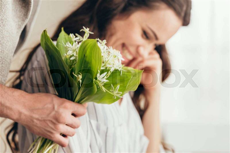 Man presenting bouquet of flowers to his smiling girlfriend at home, stock photo