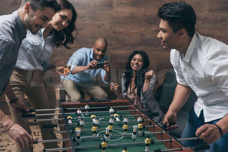 Smiling young friends playing table football together indoors , stock photo