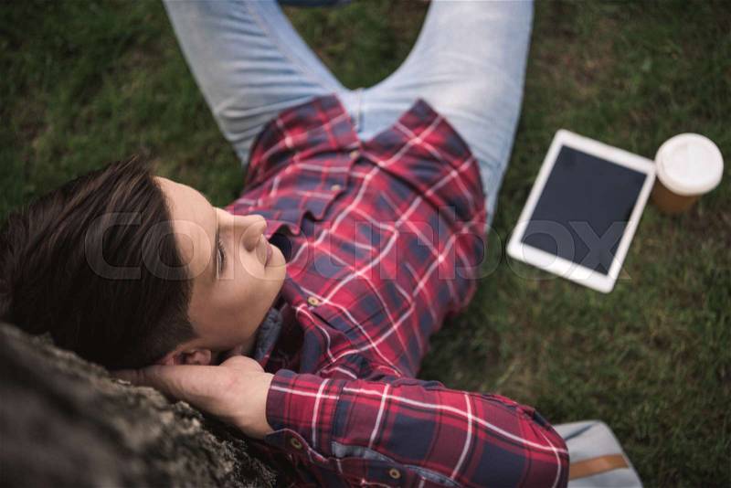 Portrait of young man leaning to tree trunk while relaxing with digital tablet and coffee, stock photo