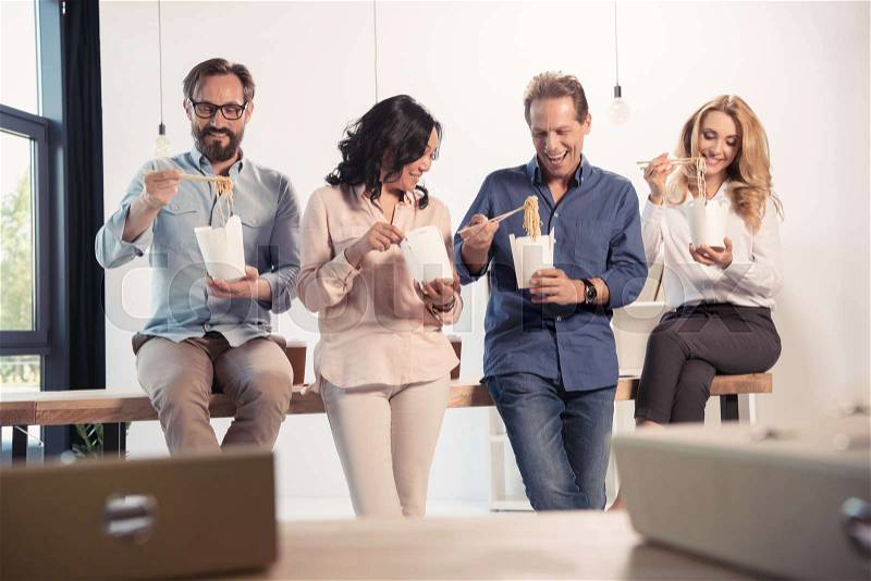 Smiling middle aged businessmen and businesswomen eating asian food in office, stock photo