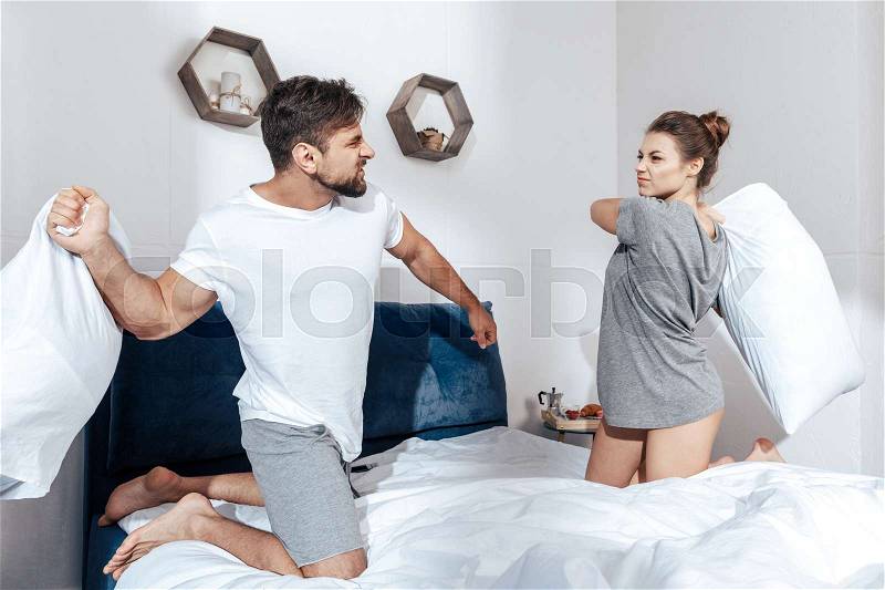 Portrait of young happy couple have battle of pillows in bed, stock photo