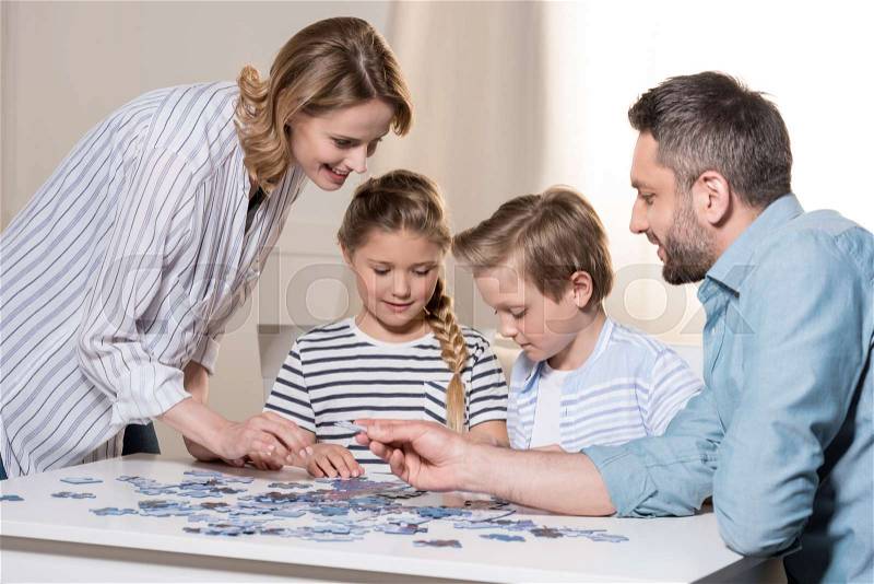 Smiling family playing with puzzle on table at home together, stock photo