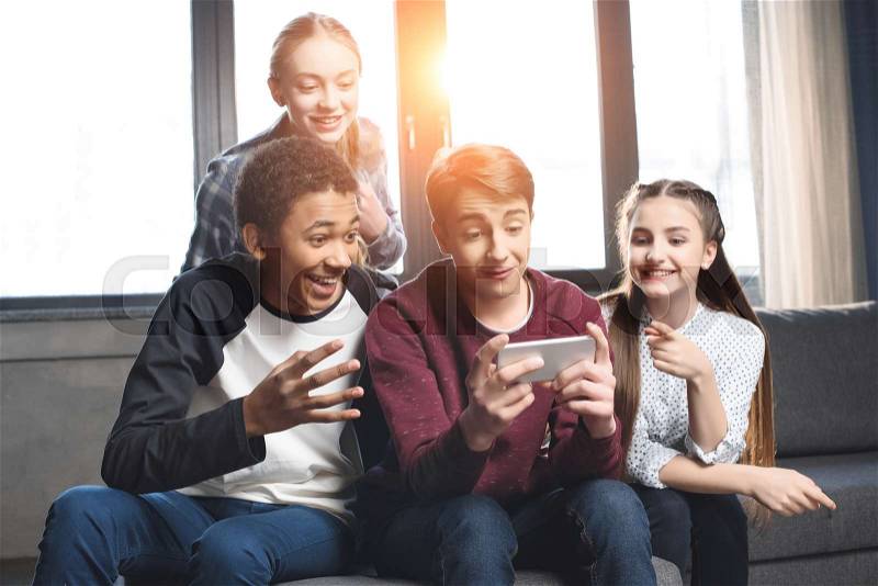 Happy multicultural teenagers group video call with smartphone and sitting on sofa at home, teenagers having fun concept, stock photo