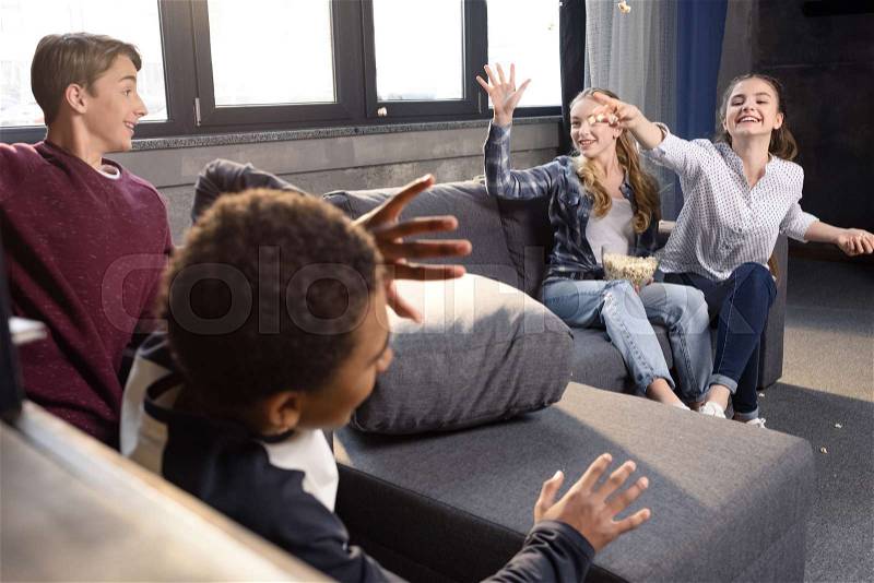 Happy group of teenagers having fun with popcorn at home, stock photo