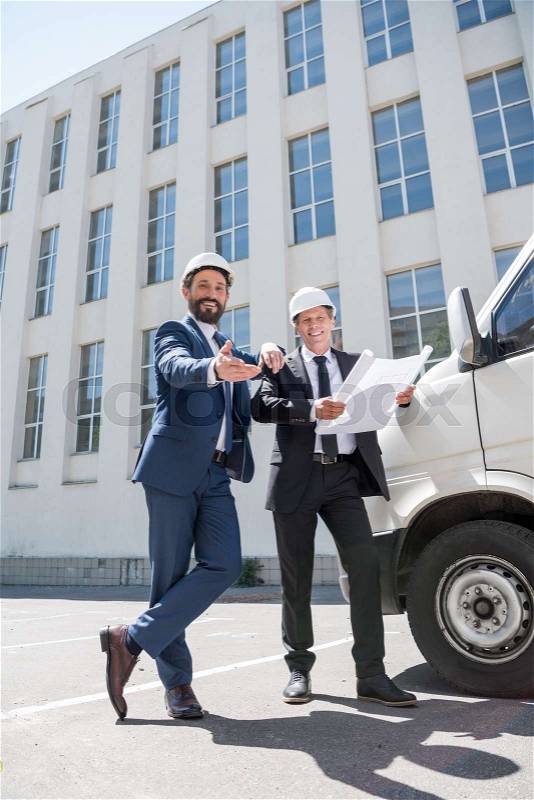 Smiling contractors in formal wear looking at camera while standing near bus outdoors, stock photo