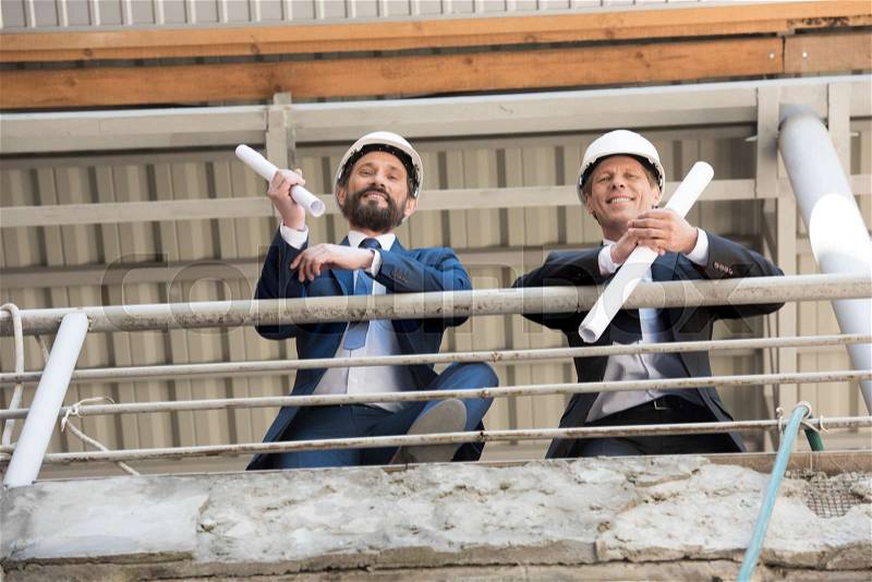Smiling contractors in suits looking at camera on construction site, stock photo