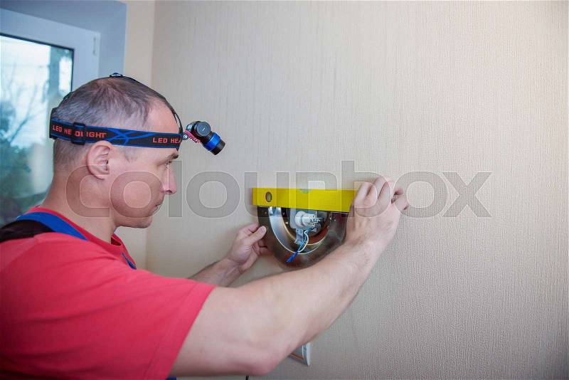 Male electrician connects the lamp on the wall, stock photo