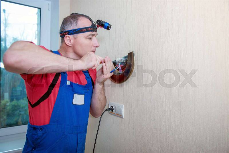 Male electrician connects the lamp on the wall, stock photo